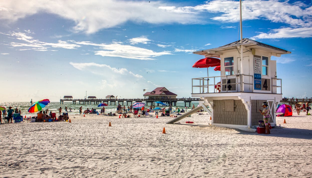 Beachgoers enjoy the summer sun at Clearwater Beach, Florida, with a scenic pier and lifeguard station.