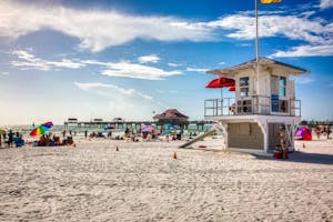 Beachgoers enjoy the summer sun at Clearwater Beach, Florida, with a scenic pier and lifeguard station.