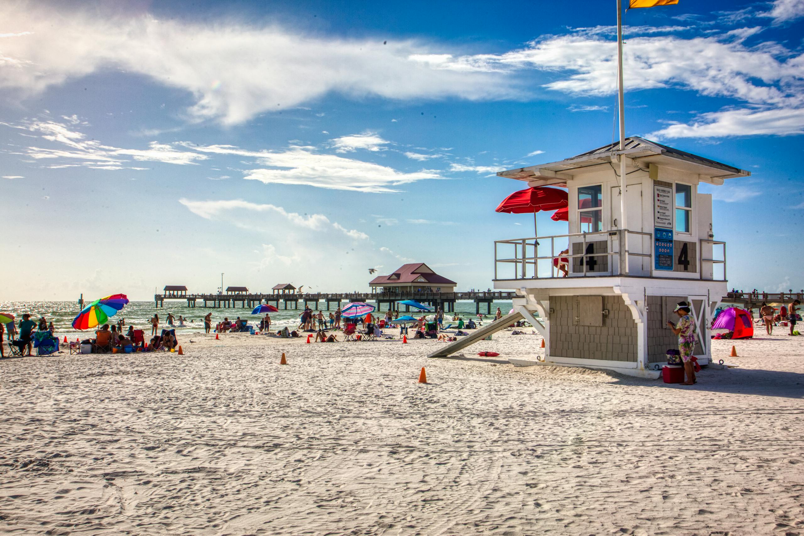 Beachgoers enjoy the summer sun at Clearwater Beach, Florida, with a scenic pier and lifeguard station.
